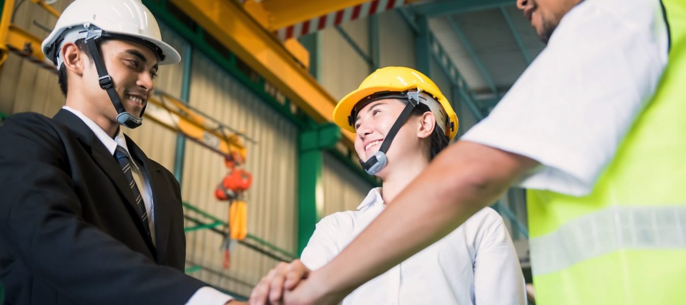 Concept of teamwork in Factory. Working team stack or gather hands together of smiling businessman, techician with safety hardhat helmet. Synergy and happyiness concept